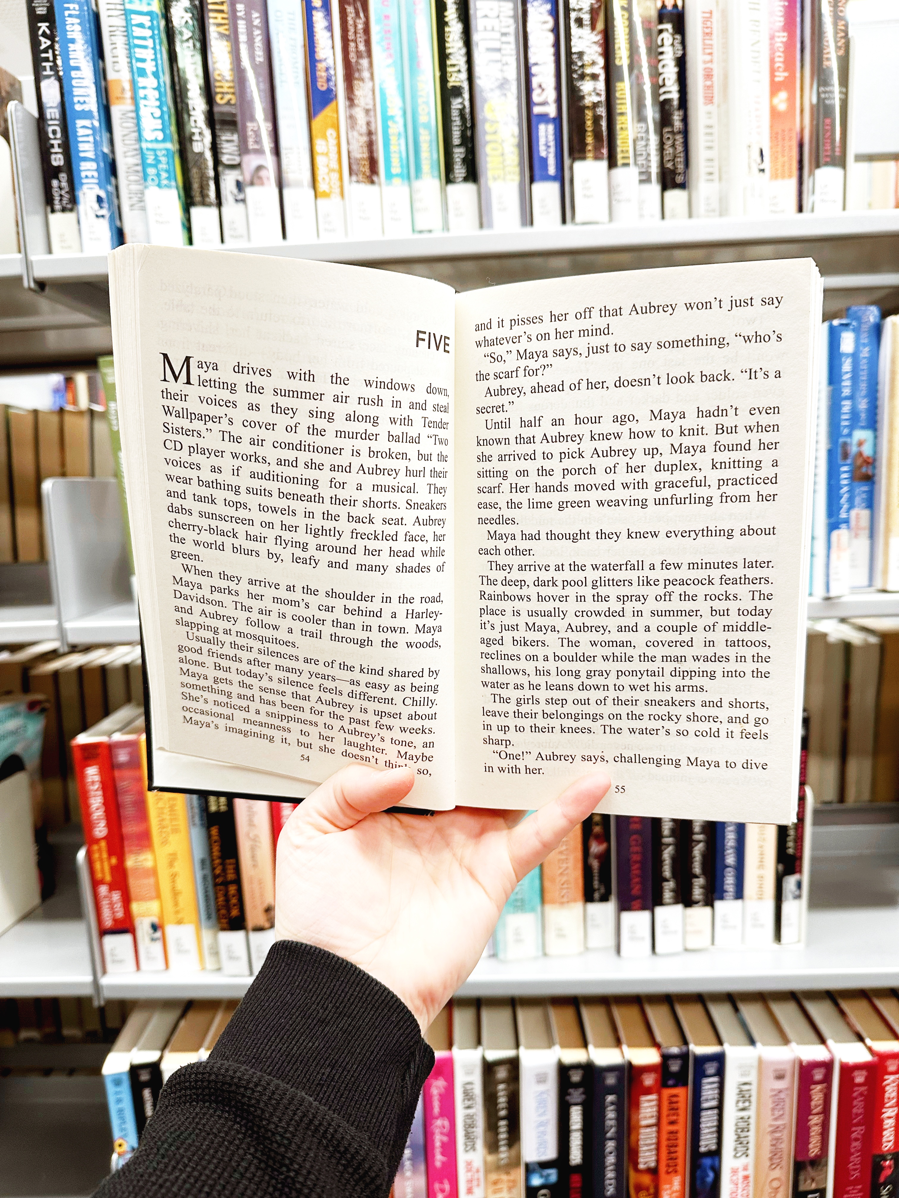 Hand holding book open in front of library bookshelf