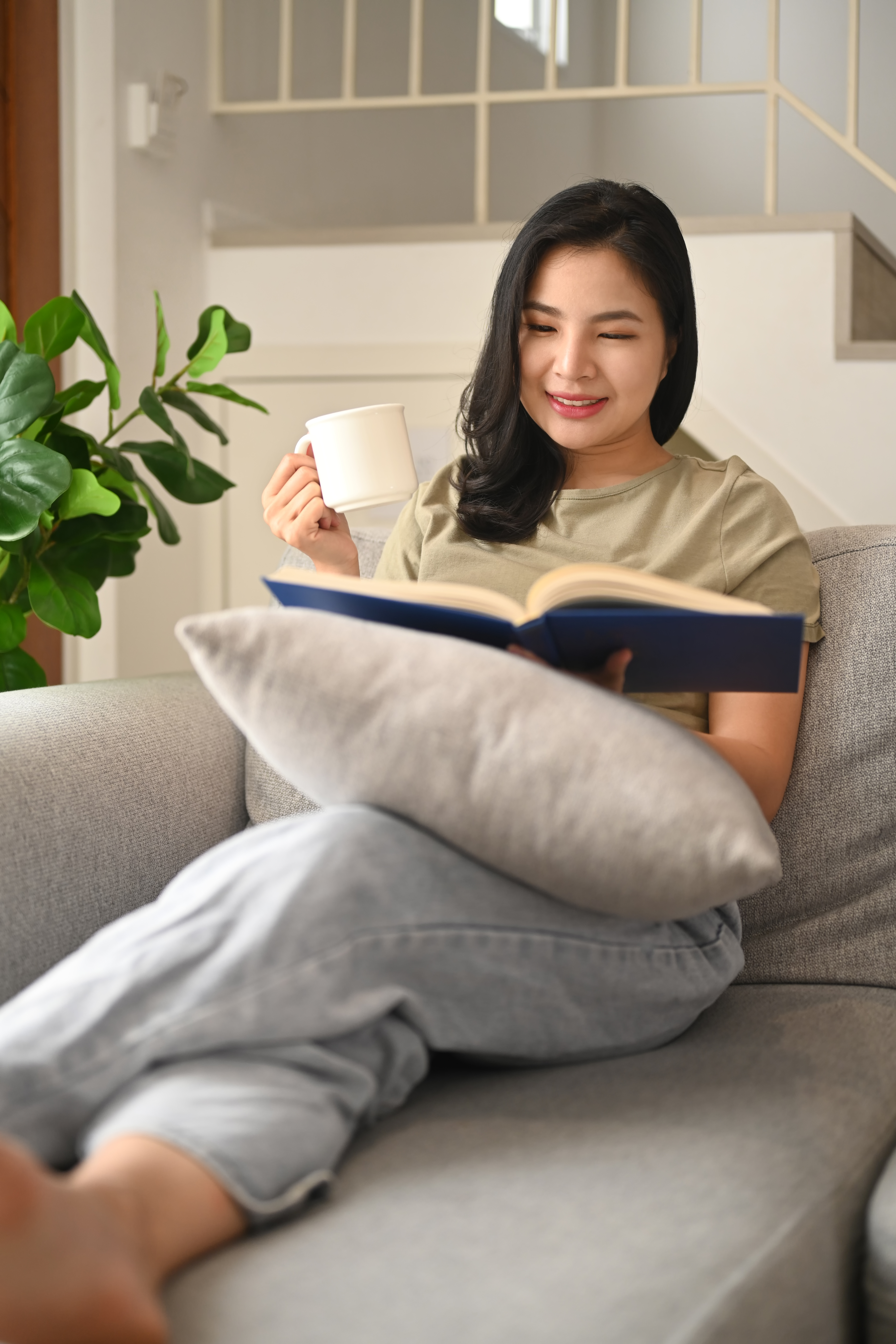 Woman drinking coffee, reading book on a couch