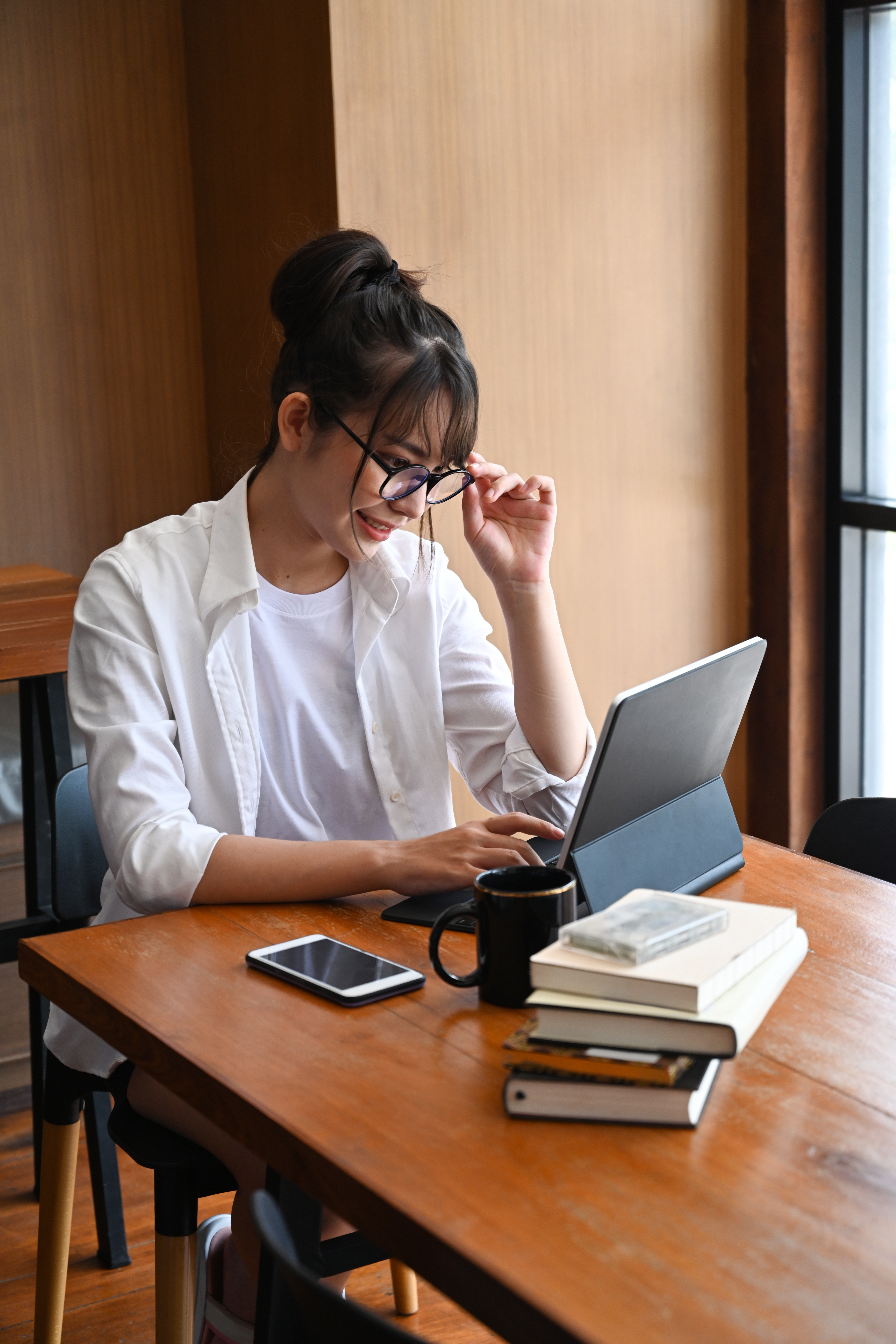 Young woman using tablet at table with mug and stack of books