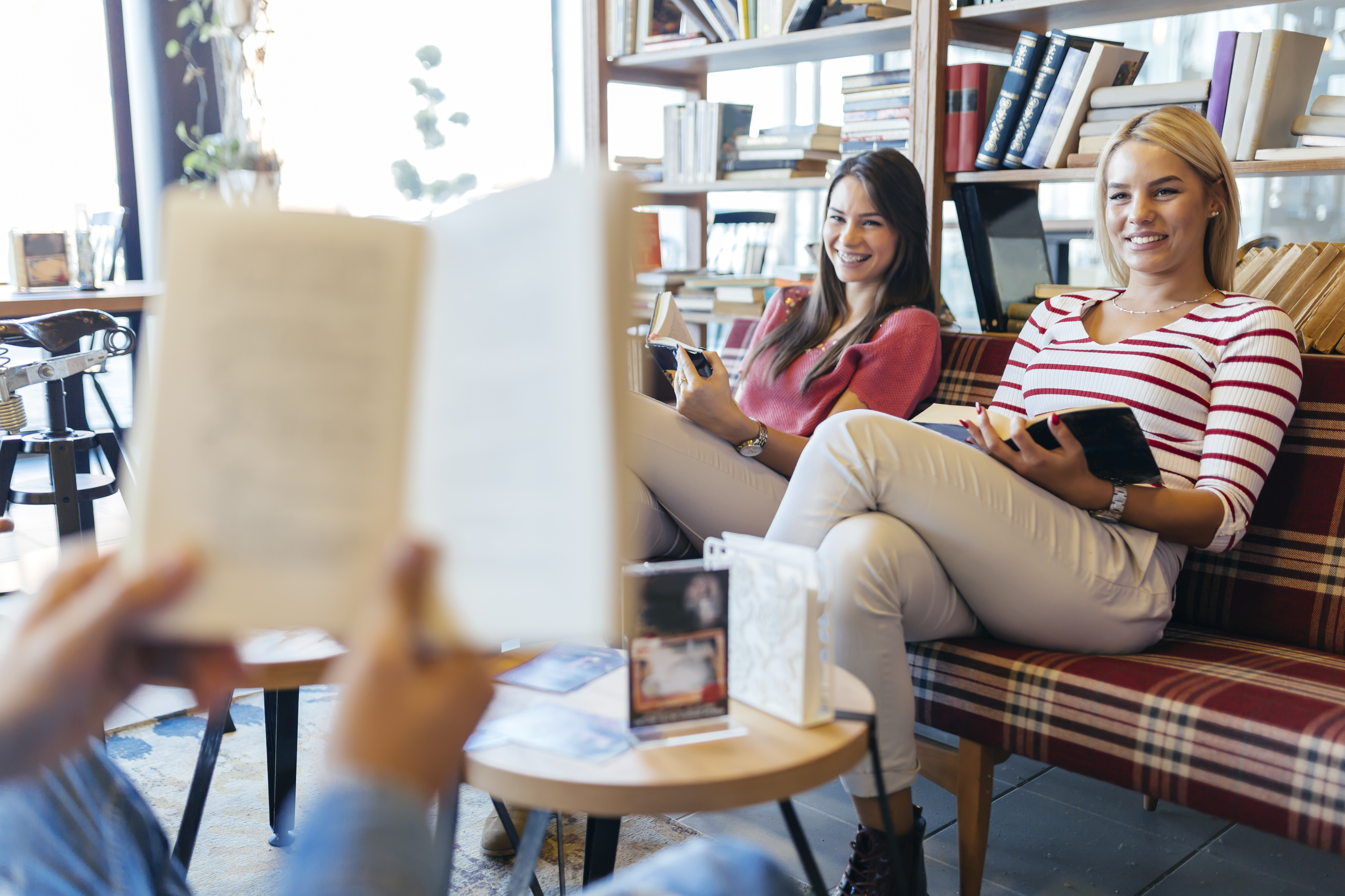 An open, blurry book in the foreground with two people sitting on a couch reading as well