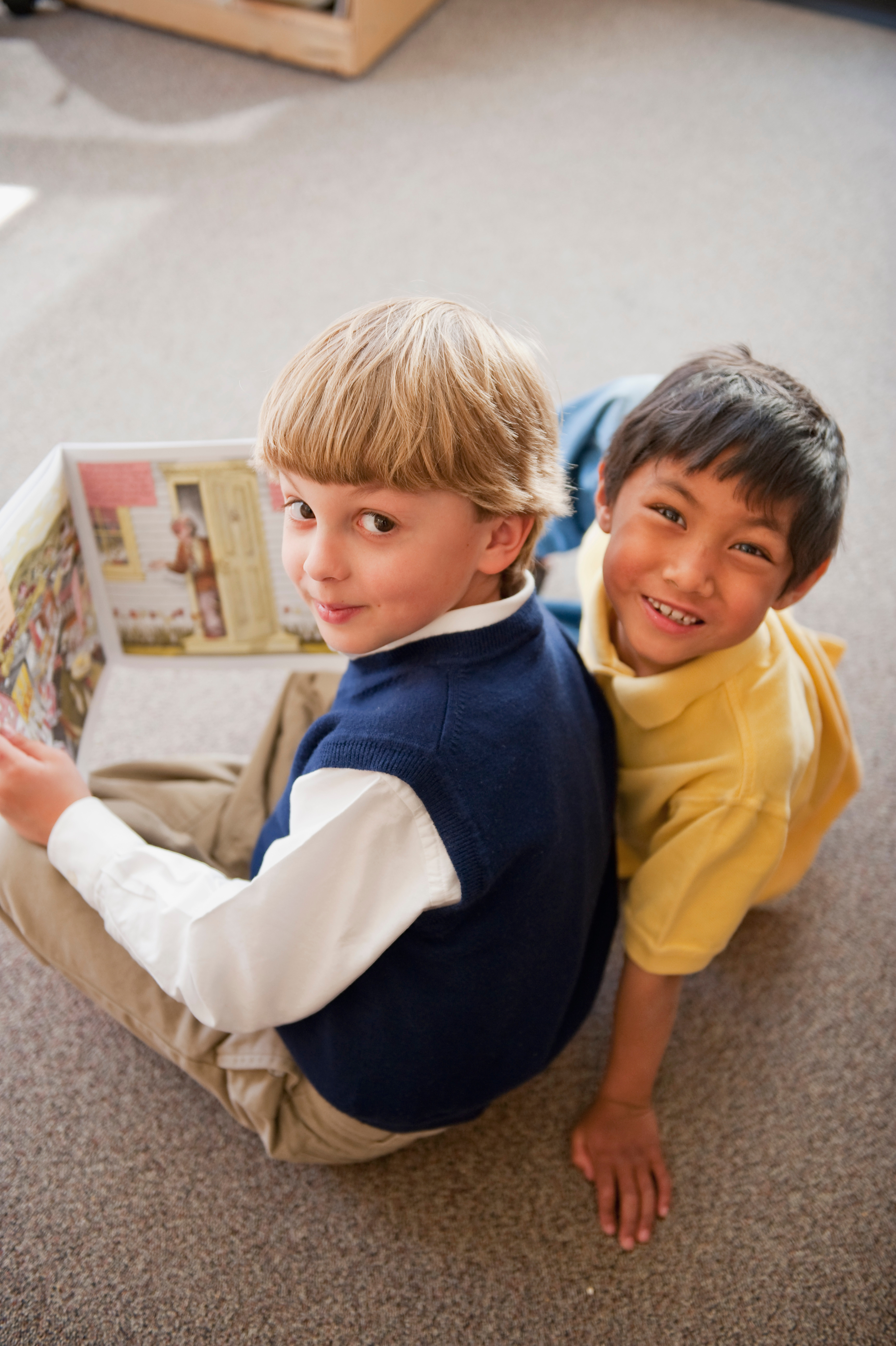 Two kids sitting on the floor reading a book